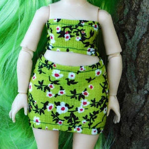 May include: A green and white floral print crop top and skirt set. The top is strapless and the skirt is a mini skirt.