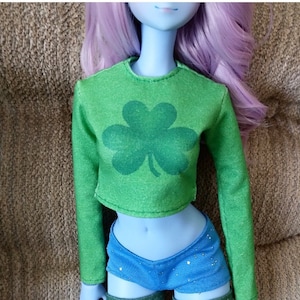 May include: A green long-sleeved shirt with a shamrock design. The shirt is cropped and has a fitted silhouette.