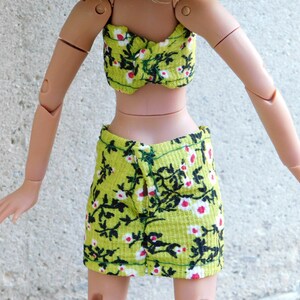 May include: A green and black floral print crop top and skirt set. The top is a strapless bandeau style and the skirt is a mini skirt with a front slit.