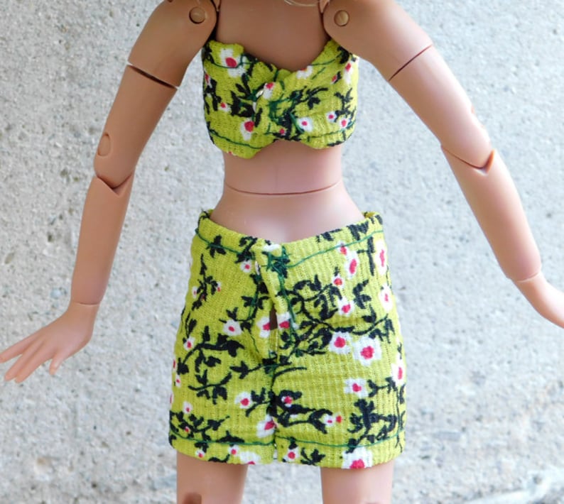 May include: A green and black floral print crop top and skirt set. The top is a strapless bandeau style and the skirt is a mini skirt with a front slit.
