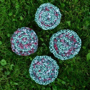 May include: Four handmade coasters made from repurposed fabric. The coasters are round and feature a spiral pattern of red and green gingham fabric.