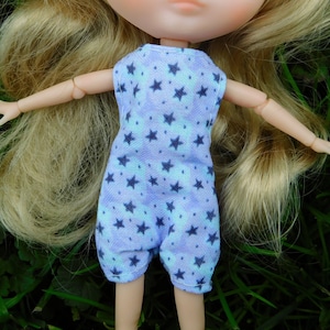 Puede incluir: Una muñeca con un mono azul claro y morado con estampado de estrellas. El mono es sin mangas y de corte holgado.