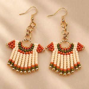 May include: A pair of gold-toned hook earrings featuring a fan-shaped design made of small beads in cream, orange, and olive green. The earrings hang from gold-toned metal rings and are finished with small gold-toned beads at the bottom.