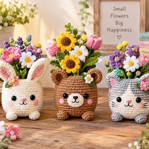 Könnte beinhalten: Drei gehäkelte Töpfe in Tierform mit bunten Garnblumen. Links ein weißer Hase, in der Mitte ein brauner Bär und rechts eine grau-weiße Katze. Jeder Topf hat schwarze Augen, rosa Wangen und einen Strauß aus Sonnenblumen, Gänseblümchen und Tulpen.