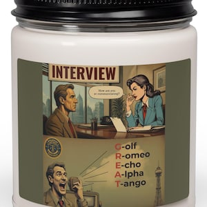 May include: A white candle in a glass jar with a black lid, featuring a label with a comic-style illustration of an interview and a phonetic alphabet graphic spelling out the word GREAT with Golf, Romeo, Echo, Alpha, and Tango.