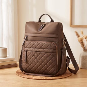May include: A brown backpack featuring a quilted front pocket with a diamond pattern, gold-tone metal zippers, a top handle, and adjustable shoulder straps. The bag has a smooth upper section and a structured design with multiple zippered compartments.
