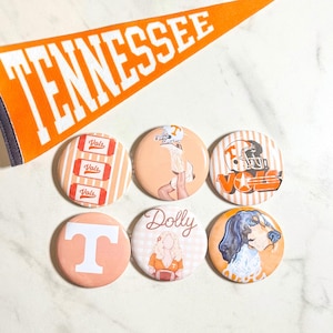 May include: Six circular pinback buttons featuring Tennessee-themed graphics, including a white letter T, a football player, a hound dog, and the name Dolly, arranged below an orange felt pennant with the white text TENNESSEE printed across it.