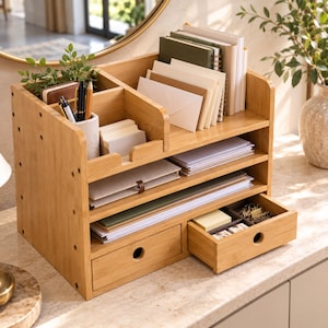 May include: A light brown bamboo desk organizer featuring multiple vertical slots for notebooks and envelopes, horizontal shelves for paper documents, a cylindrical pen holder, and two small drawers with circular cutouts for small office supplies.