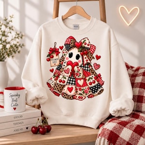 May include: A cream-colored crewneck sweatshirt featuring a central graphic of a ghost made of patchwork fabric patterns including cherries, leopard print, and gingham. The ghost wears a large bow and holds a red heart, with a tag labeled PATCHWORK GHOST.