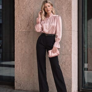 May include: A pale pink satin long-sleeve blouse with a high collar, button-down front, and gathered cuffs paired with black high-waisted trousers, a thin black belt, and a matching pale pink clutch bag with a soft, gathered texture.
