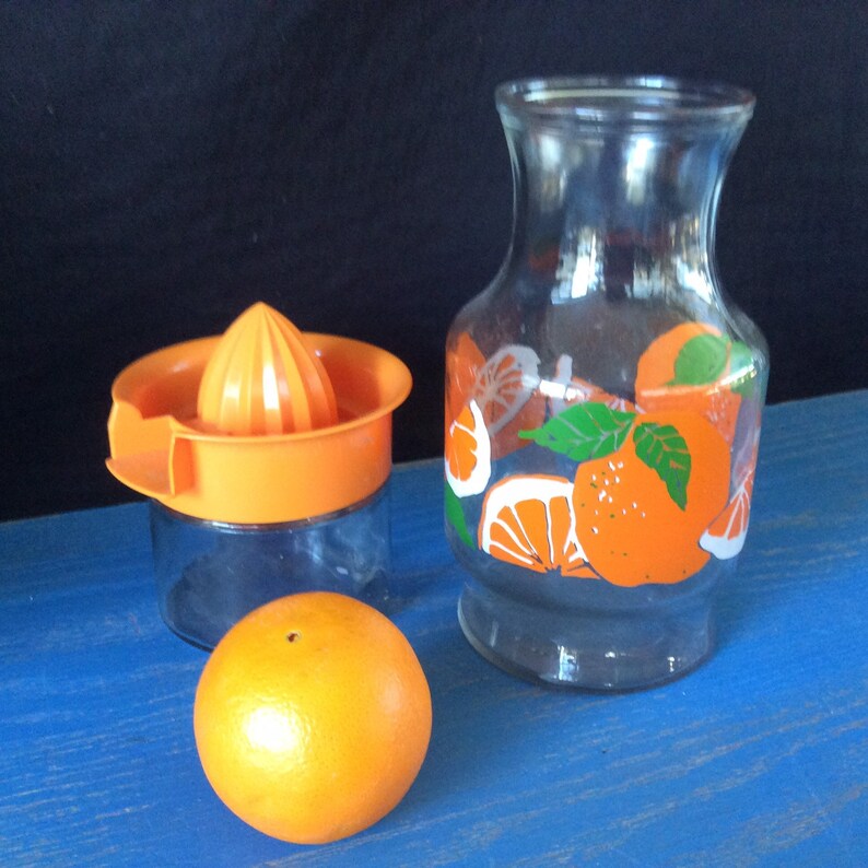 Pu&ograve; includere: Un set di strumenti per fare il succo d'arancia, tra cui una caraffa di vetro con un design a fette d'arancia, uno spremiagrumi di vetro e un'arancia intera.