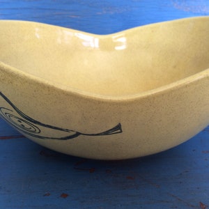 May include: A yellow ceramic bowl with a black and white banana design. The bowl has a speckled finish and a wide, rounded shape.