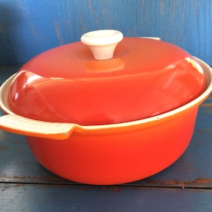 May include: Orange enamel cast iron Dutch oven with a white lid knob. The oven has two white handles.