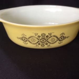 May include: A yellow ceramic baking dish with a black floral design. The dish is oval shaped and has a white interior.