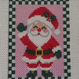 May include: A needlepoint canvas featuring a Santa Claus figure with a red hat, red coat, black belt with a yellow buckle, and black boots. The figure is set against a pink background and framed by a black and white checkered border.