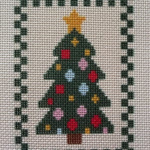 May include: A cross-stitch embroidery on light-colored fabric featuring a dark green Christmas tree with a yellow star on top. The tree is decorated with small red, pink, light blue, and yellow squares. A dark green checkered border frames the design.