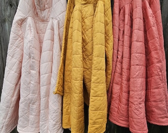 May include: Three quilted jackets in different colors: pink, yellow, and red. The jackets have a hood and are hanging on a wooden fence.