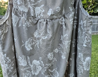 May include: A sleeveless, taupe-colored top with a white floral pattern. The fabric has a subtle sheen, and the design features large, stylized flowers and foliage. The top has a gathered detail at the neckline.