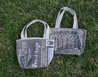 May include: Two gray canvas tote bags with white handles. One bag features a vintage design with the text "Coarse Wool Cotton, Reg.U.S.Pat.Off. Made in Every Spool, Feed dogs, Needles". The other bag features a vintage design with the text "Celebrated Shears, Shears for Cutting Curling Hooks".