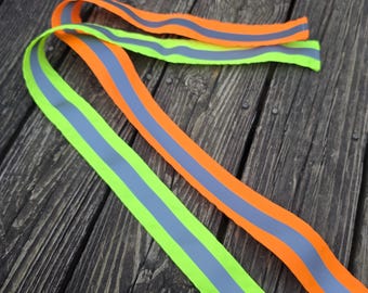 May include: Two long, flexible fabric strips featuring high-visibility colors. One strip is bright neon orange and the other is neon yellow-green. Each strip has a wide, centered silver reflective stripe running along its entire length.