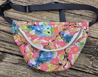 May include: A pink fanny pack with a colorful owl and floral pattern. The bag has a gray adjustable strap and a white zipper. The owl design features blue, yellow, and green colors. The bag is made of fabric.