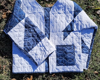 May include: A quilted jacket in shades of white and blue, featuring a geometric pattern. The jacket has a V-neck design, long sleeves, and a patch pocket. The fabric is quilted with a wavy stitch.