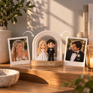 Puede incluir: Un adorno para pastel de bodas personalizado con dos figuras pequeñas de una novia con vestido blanco y un novio con traje negro bajo un arco blanco. La base es de color canela con el texto Emma & Daniel impreso en blanco al frente.