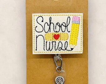 Könnte beinhalten: Ein rechteckiger Ausweishalter mit einem gestickten Aufnäher, der den Text School Nurse, ein beiges Pflaster mit einem roten Herz und einen gelben Bleistift zeigt. Der Aufnäher ist an einem transparenten Clip befestigt und auf einer braunen Karte.