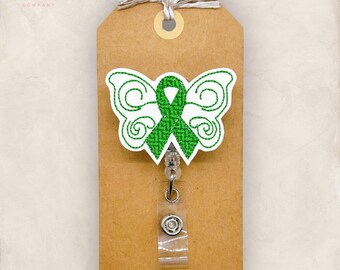 May include: A badge reel featuring a white butterfly shape with green embroidered swirl details and a central green awareness ribbon. The badge reel is attached to a rectangular brown card with a white string tied at the top hole.