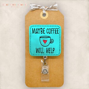 May include: A teal badge reel with the text "MAYBE COFFEE WILL HELP" and a coffee cup graphic with a red heart. The badge is attached to a brown tag with a twine bow.