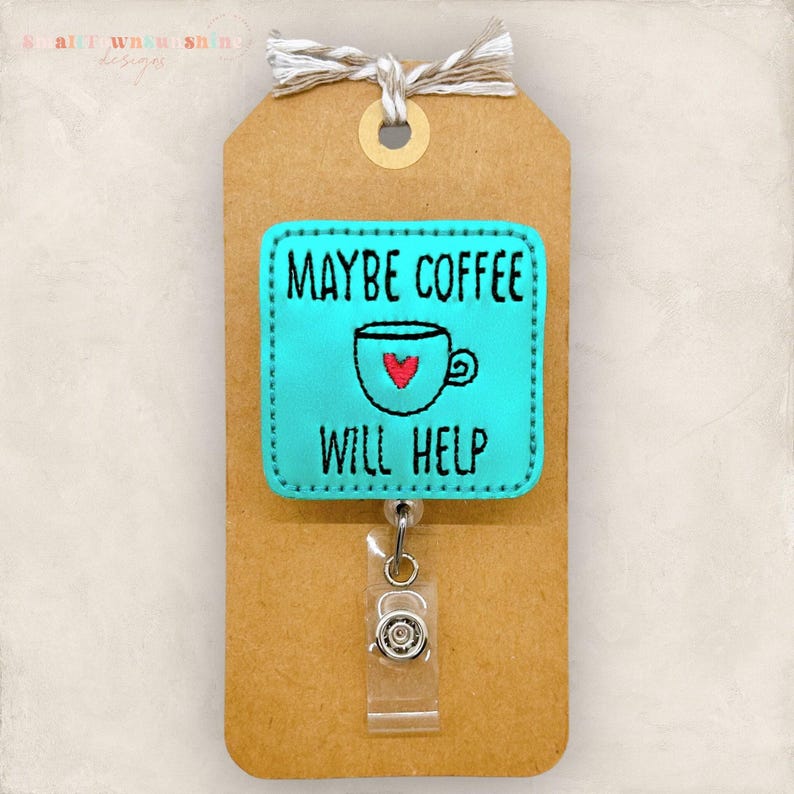 May include: A teal badge reel with the text "MAYBE COFFEE WILL HELP" and a coffee cup graphic with a red heart. The badge is attached to a brown tag with a twine bow.