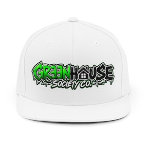 May include: A white snapback cap featuring a graffiti-style logo on the front. The logo displays the text GREENHOUSE SOCIETY CO. in a vibrant green and black colour scheme, with a small house icon integrated into the letter H.
