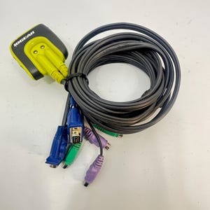 May include: An IOGEAR KVM switch cable assembly featuring a black and lime green connector housing with the brand name printed in white. The unit includes a long, coiled dark gray cable that branches into multiple blue, green, and purple connectors.