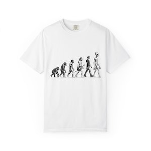 May include: A white short-sleeved t-shirt featuring a black and white graphic print of the human evolution sequence, starting with a primate and progressing through various hominid stages to a modern human, ending with an extraterrestrial figure.