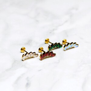 May include: Four gold-tone stud earrings featuring a curved, fan-like design. Each earring is set with five marquise-cut stones in clear, red, dark green, and iridescent white colors, attached to a flat circular backing post.