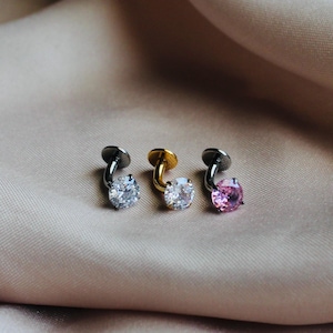 May include: Three labret piercings with flat back discs and prong-set round gemstones. The left piece is silver-toned with a clear stone, the center is gold-toned with a clear stone, and the right piece is silver-toned with a pink gemstone.