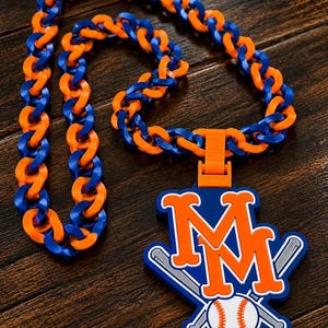 May include: A chunky plastic chain necklace featuring alternating bright orange and royal blue links. Attached is a large pendant displaying the orange letters MM above a white baseball with orange stitching, crossed by two grey baseball bats.