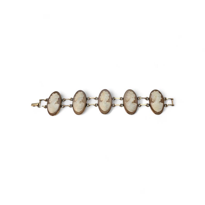 May include: A vintage bracelet featuring five oval cameo pendants. Each cameo showcases a profile portrait in a cream color, set in a gold-toned metal frame. The bracelet is connected by small gold-toned links and has a clasp closure.