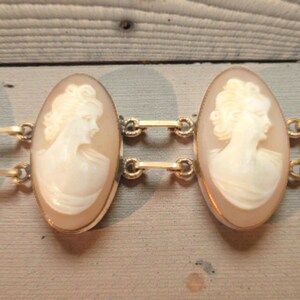 May include: A vintage gold-tone bracelet featuring oval cameo pendants. Each cameo displays a profile of a woman in relief, set within a gold frame. The bracelet is connected by small gold links, showcasing classic jewelry design.