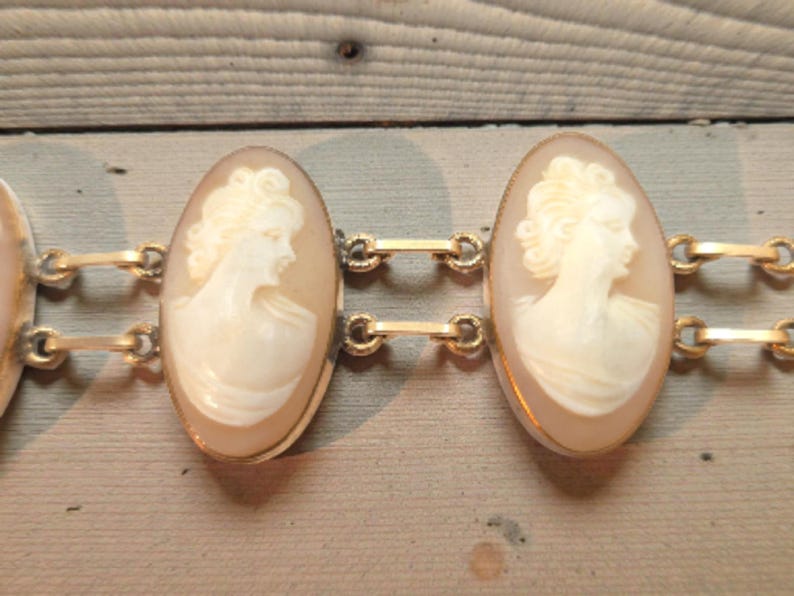 May include: A vintage gold-tone bracelet featuring oval cameo pendants. Each cameo displays a profile of a woman in relief, set within a gold frame. The bracelet is connected by small gold links, showcasing classic jewelry design.