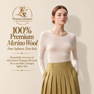 May include: A long-sleeved, cream-colored crew neck sweater made of 100% merino wool, paired with a high-waisted, olive green pleated skirt. Text on the image includes PlumaCashmere, 100% Premium Merino Wool, Pure Softness. Zero Itch.