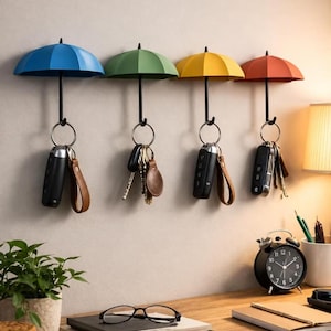 May include: Four wall-mounted key hooks shaped like miniature umbrellas in blue, green, yellow, and red. Each umbrella hook features a black handle that extends downward to hold a metal ring with various keys and key fobs attached to them.