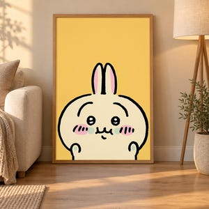 May include: A framed wall art print featuring a cartoon rabbit character with long ears, large black eyes, and pink blush on its cheeks. The character is rendered in a simple black outline against a solid, bright yellow background.