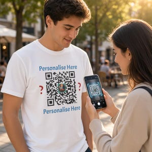 May include: A white short-sleeved t-shirt featuring a large black and white QR code printed on the chest. The text "Personalise Here" is printed in blue above and below the QR code, with red question marks on the left and right sides.
