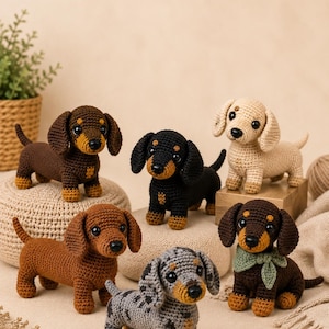 May include: A collection of six crocheted dachshund figurines in various colours including dark brown, black and tan, light cream, medium brown, grey dapple, and a dark brown dog wearing a small green fabric neckerchief, all with black eyes.