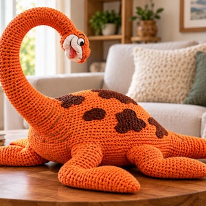Puede incluir: Un dinosaurio de peluche tejido a ganchillo en color naranja brillante con manchas marrón oscuro. La criatura presenta un cuello largo y curvado, una cara sonriente con una pequeña lengua rosa y cuatro patas robustas, todo en punto texturizado.