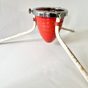 Puede incluir: Un soporte para árbol de Navidad de metal rojo y blanco con tres patas. El soporte tiene una parte superior cromada y una base de metal roja.