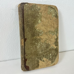 Op de afbeelding: Een klein, versleten, groen en bruin boek met een textuur.