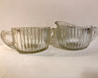 Peut inclure: Un ensemble sucrier et crémier en verre transparent avec des motifs nervurés verticaux et des poignées.