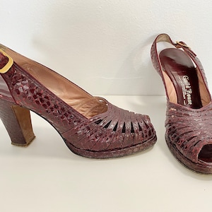 May include: A pair of burgundy snakeskin heeled shoes with a peep toe and an ankle strap. The shoes are labeled "Guild House" on the inside.